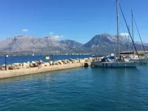 Sailing yachts moored at a stone pier, with bare mountains across the water