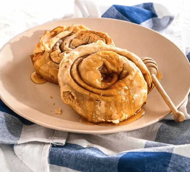 Two spiral pastry pies drizzled with honey on a plate with a checked cloth