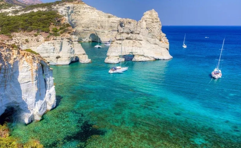 Sailing yachts anchored among white rock arches in turquoise water