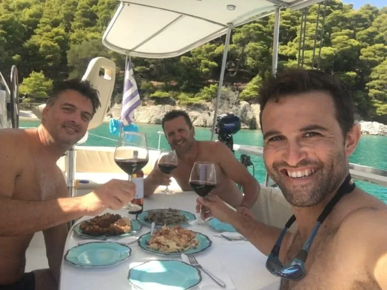 Three friends raising glasses of red wine at a lunch table on a catamaran