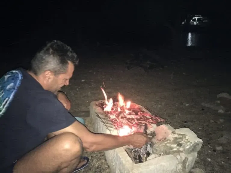 Man grilling at night over a stone-built barbecue on a beach
