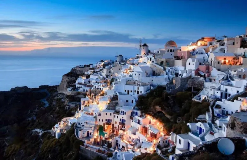 White houses of Oia on Santorini lit up at dusk, windmills on the ridge