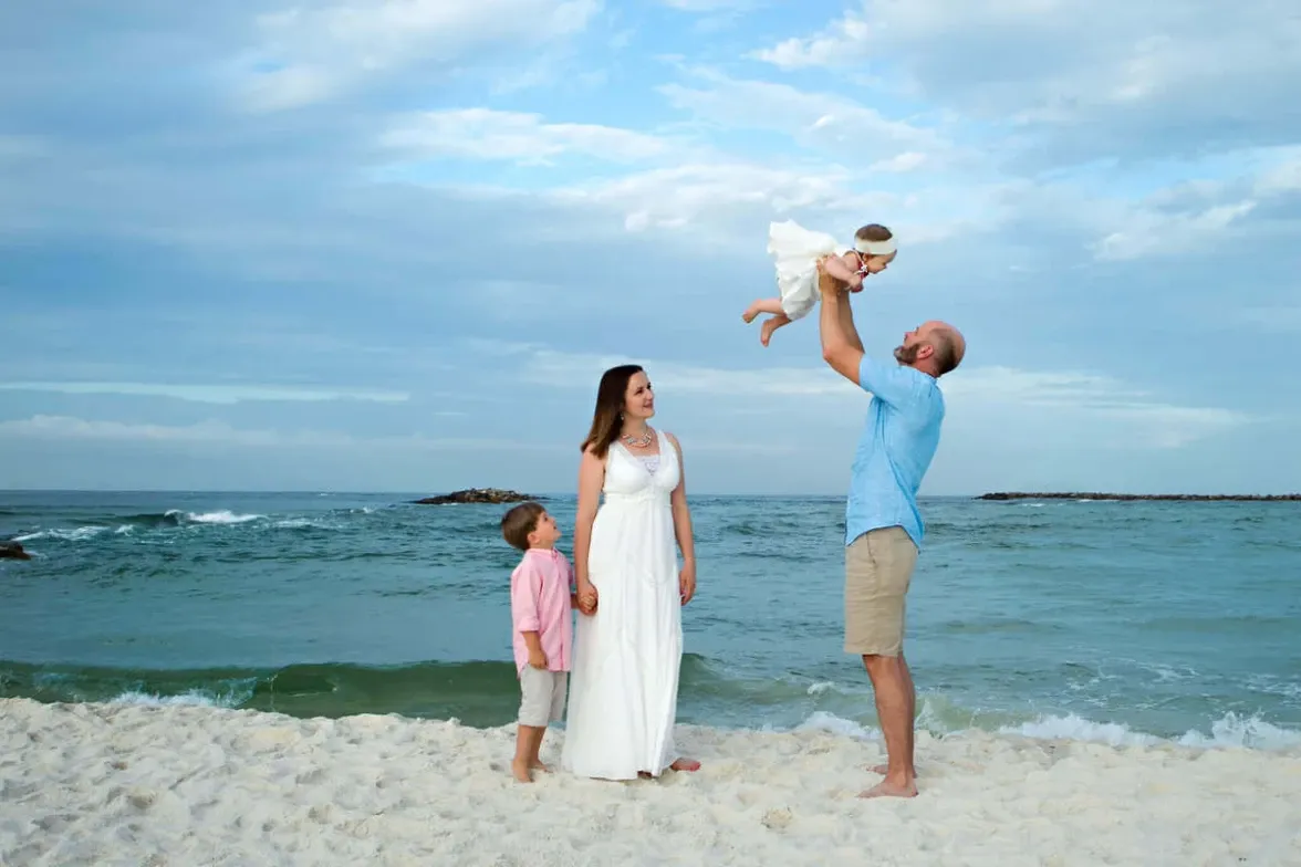 Family on a white sand beach, the father lifting a baby into the air