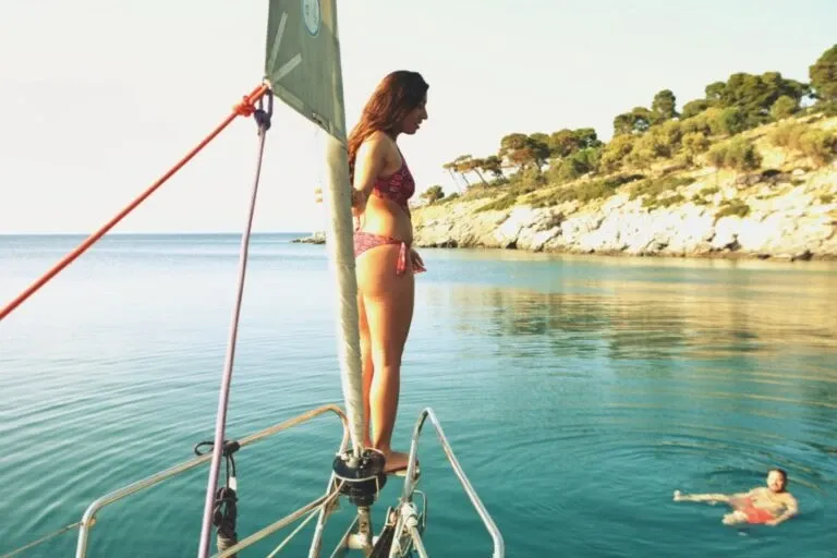 Woman standing on the bow of a yacht in a calm cove, a swimmer in the water below
