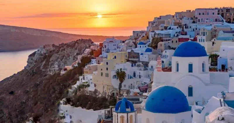 Sun setting over the Santorini caldera behind blue domes and white houses