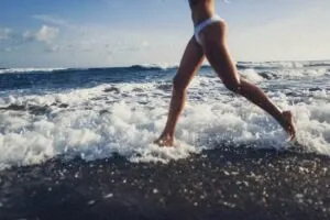 Legs of a woman running through foaming waves on a dark sand beach