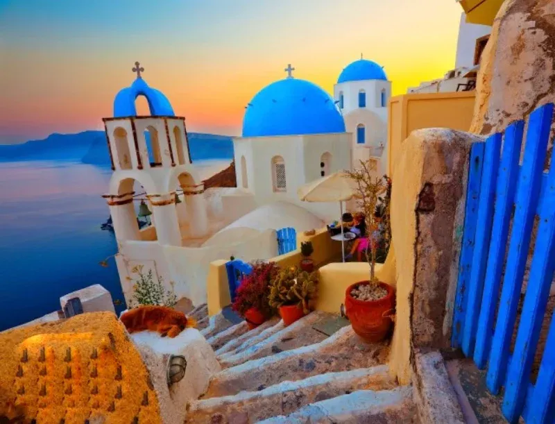 Blue-domed church and bell tower above whitewashed steps and a blue gate at sunset