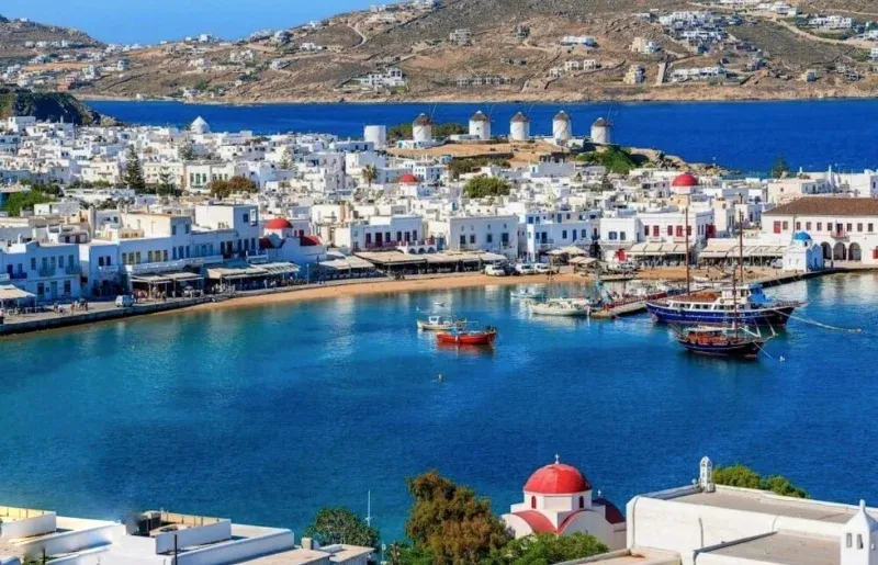 Row of windmills above the white houses and moored boats of Mykonos harbour