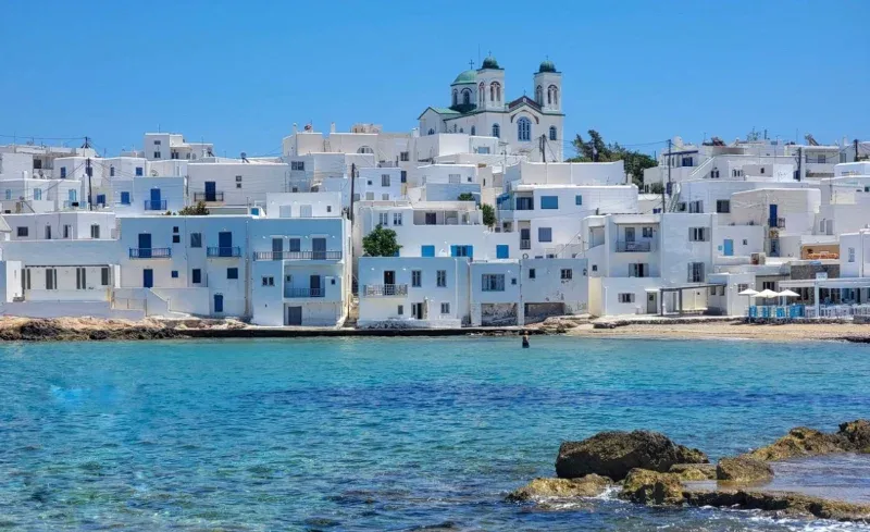 White houses and a twin-towered church above a turquoise bay on Paros