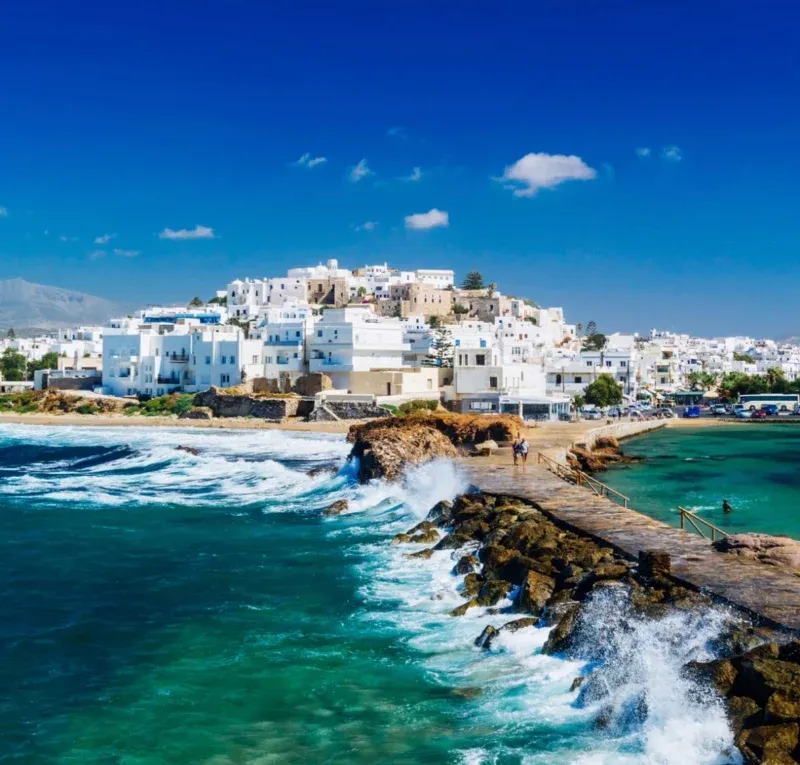 Waves breaking against the causeway below the white houses of Naxos town