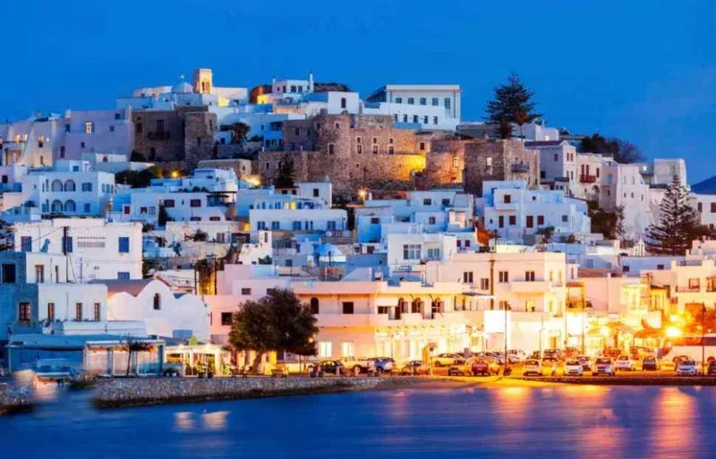 Naxos town and its hilltop castle lit up at dusk above the harbour