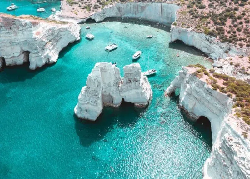 Boats in turquoise water among white rock arches off Milos, seen from above