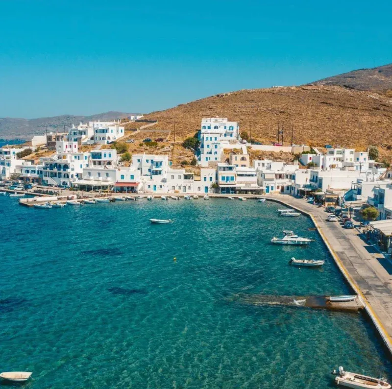 White houses around a small harbour with boats below a bare hillside on Tinos