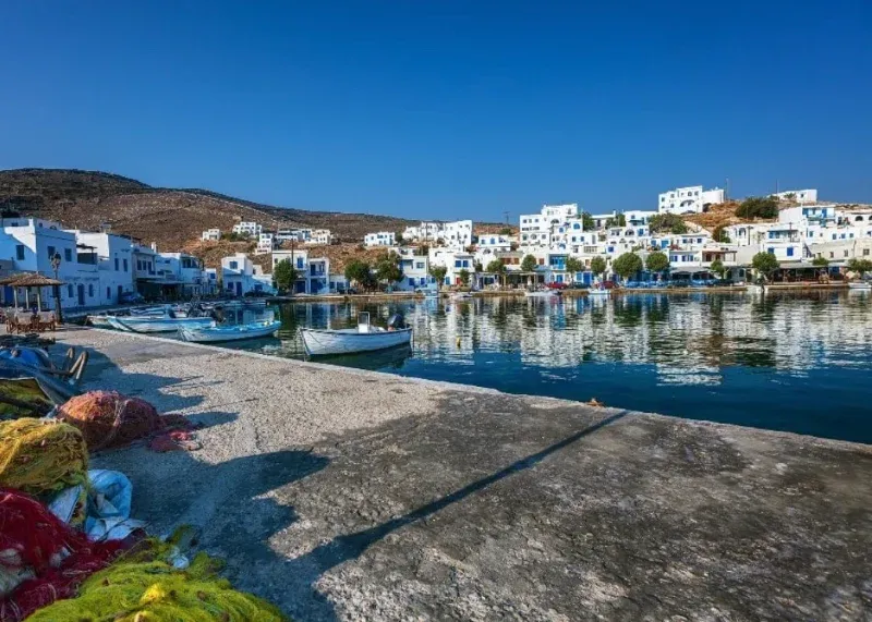 Fishing nets on a quay beside a white village reflected in a calm harbour