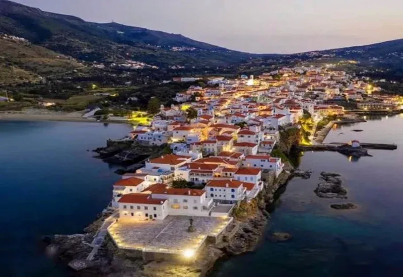 Andros town lit up at dusk on its narrow peninsula between two bays