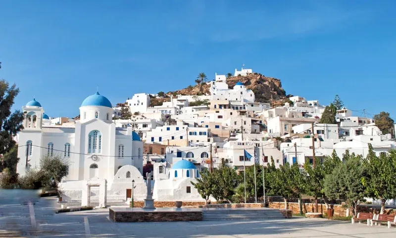 Blue-domed white church on a square below the hilltop village of Ios