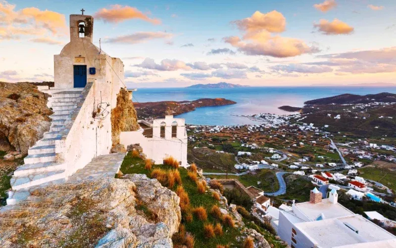 Whitewashed chapel with steps above a valley and a bay at sunset