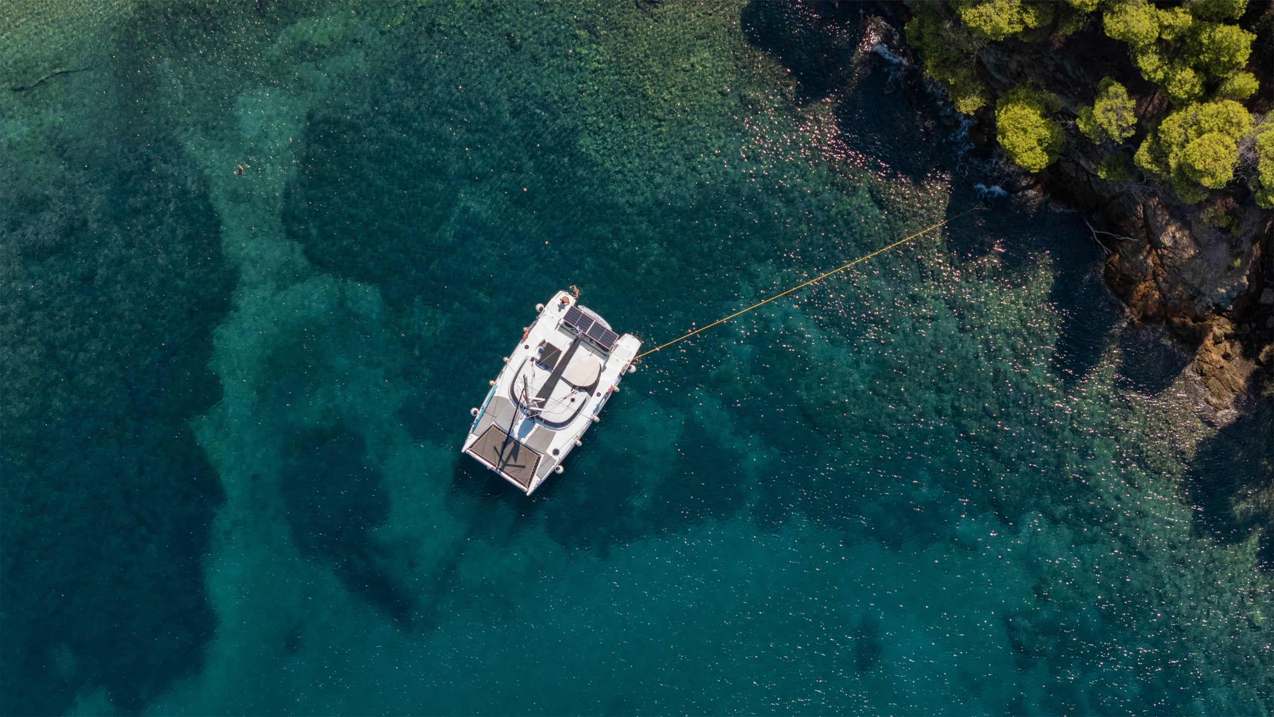Catamaran moored off a rocky pine shore in clear green water at Agia Kyriaki