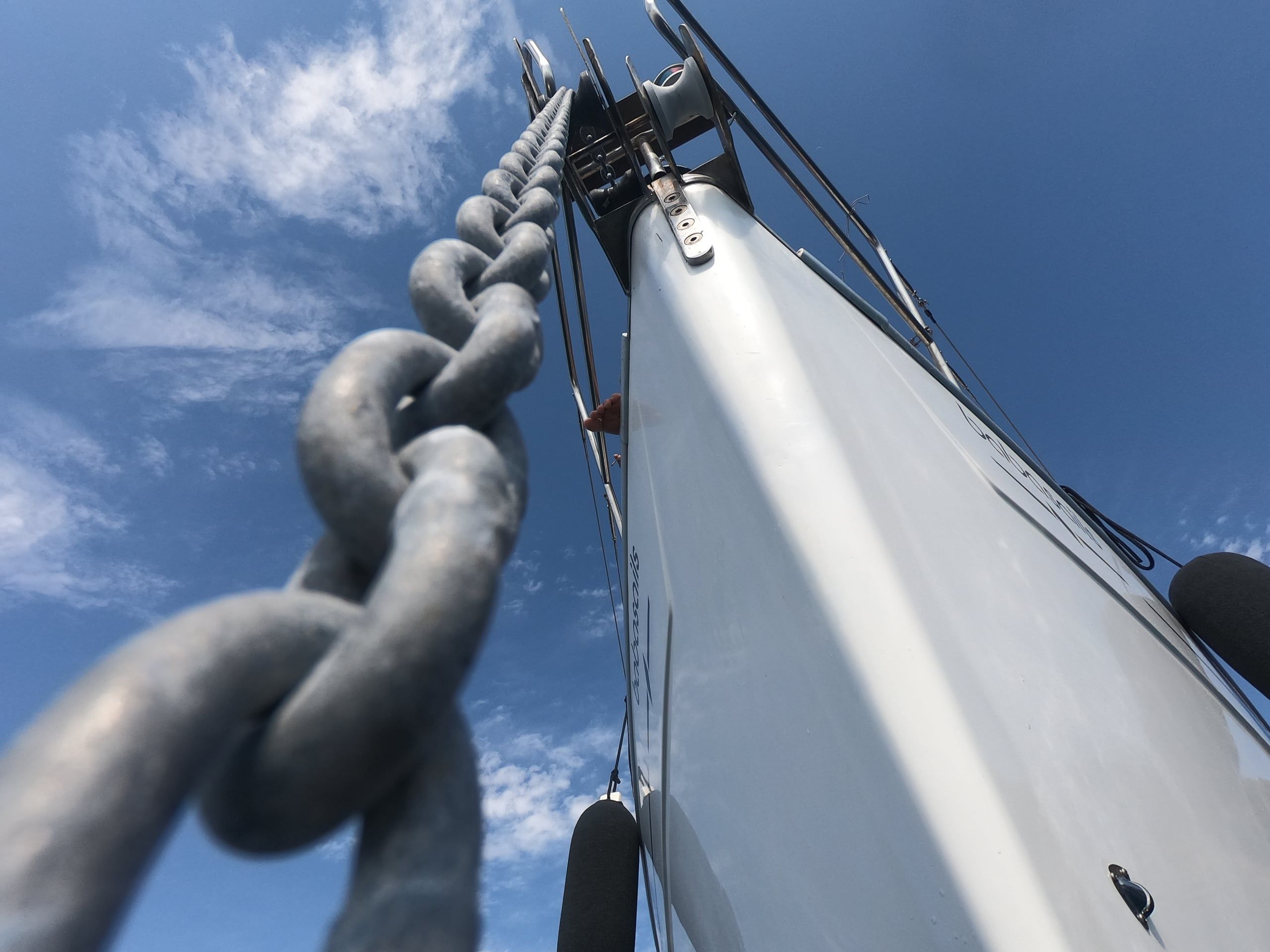 Anchor chain rising to the bow of a sailing yacht under a blue sky