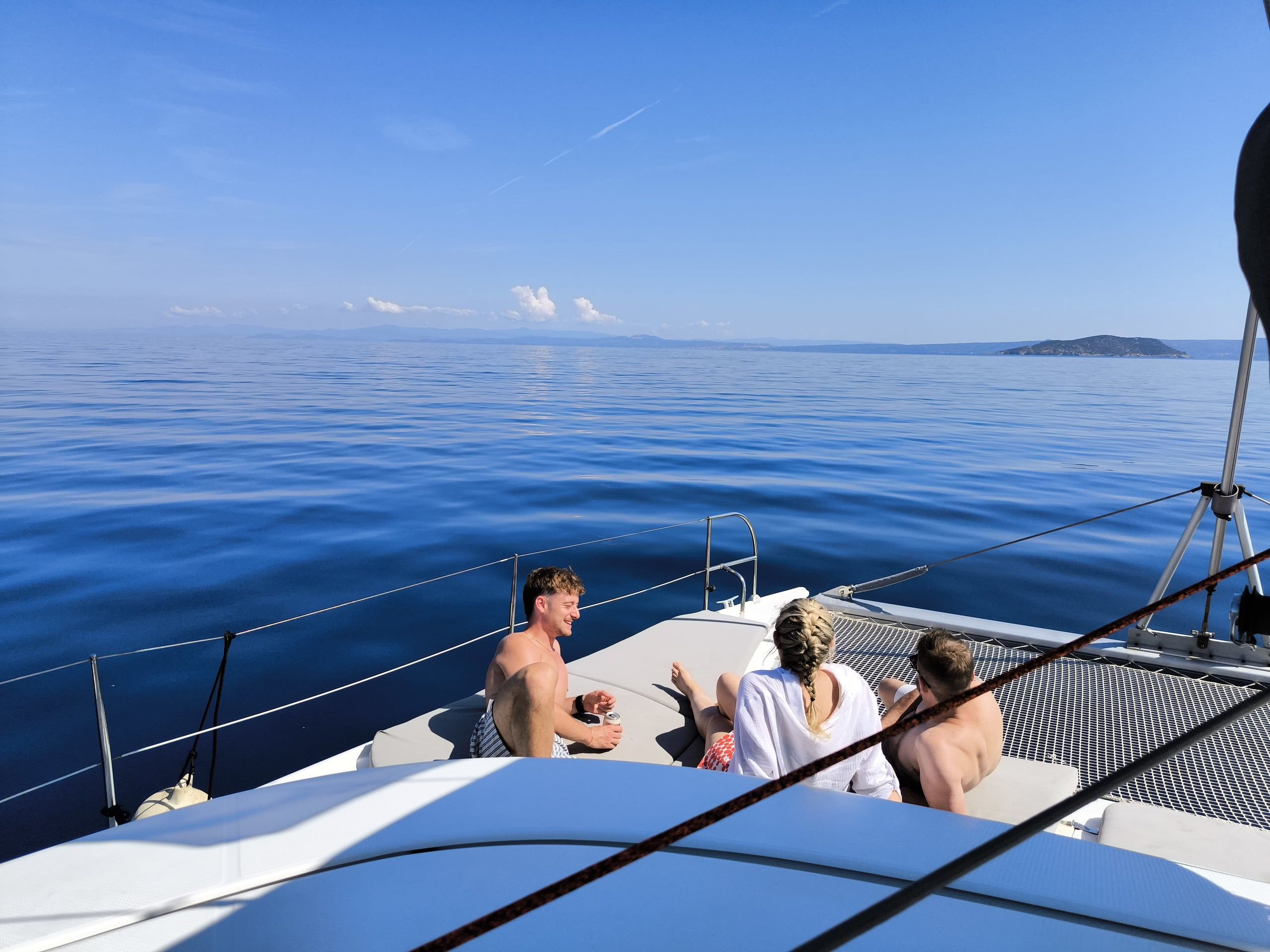Friends on a catamaran’s bow on a calm open sea, an islet in the distance