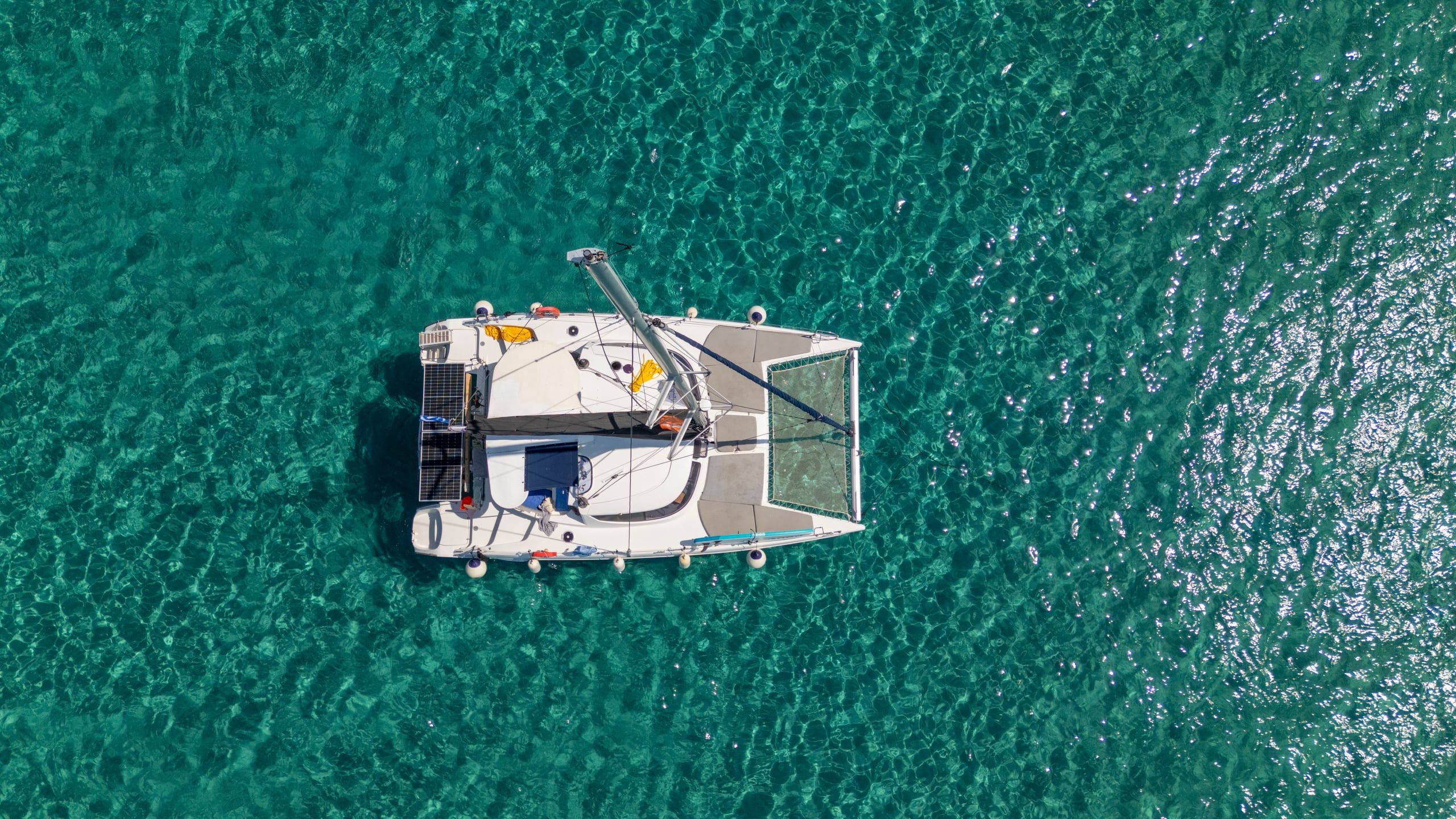 Top-down view of a catamaran deck and trampoline net over turquoise water