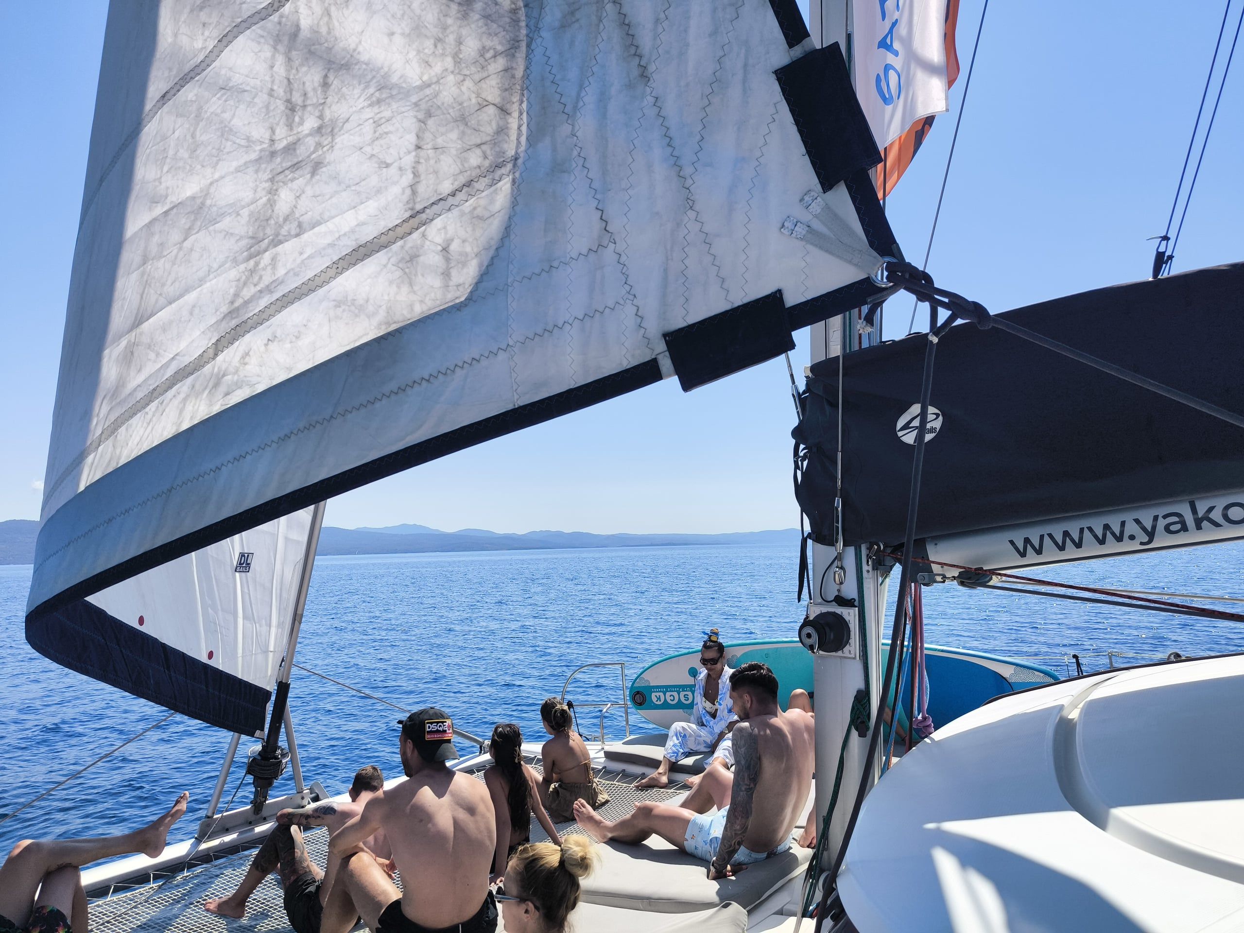 Guests relaxing on a catamaran’s nets and deck under the genoa at sea