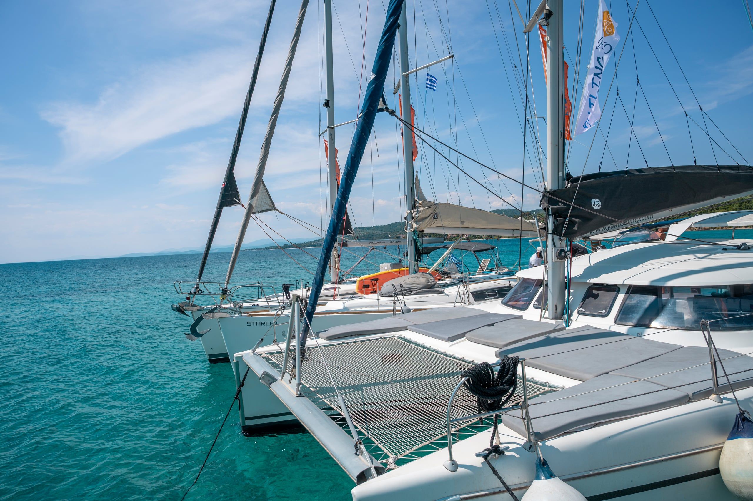 Catamaran rafted alongside sailing yachts in turquoise water under a blue sky