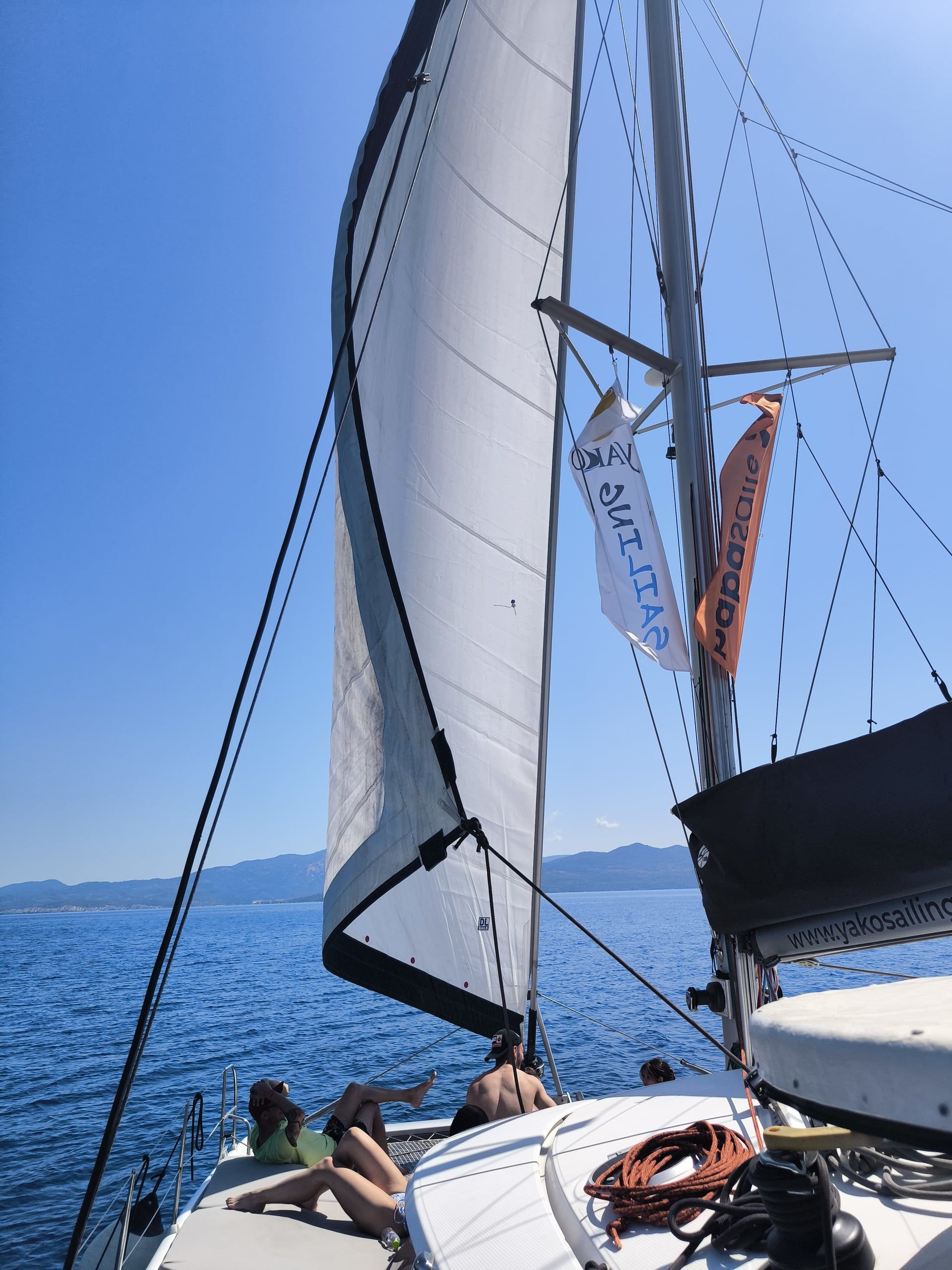 Guests lying on a catamaran’s bow as it sails under the genoa