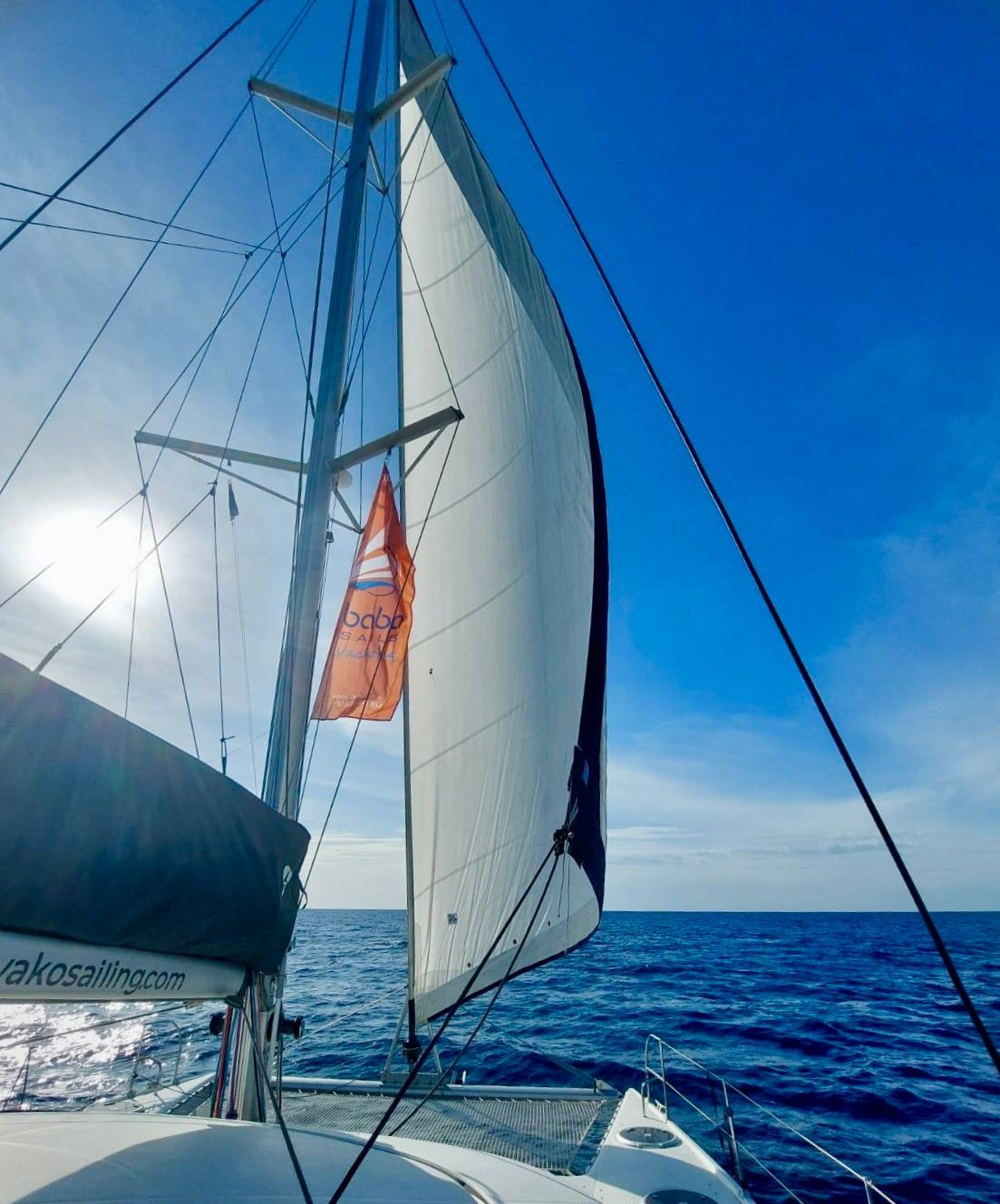 Catamaran under full sail on a deep blue sea, seen from its deck