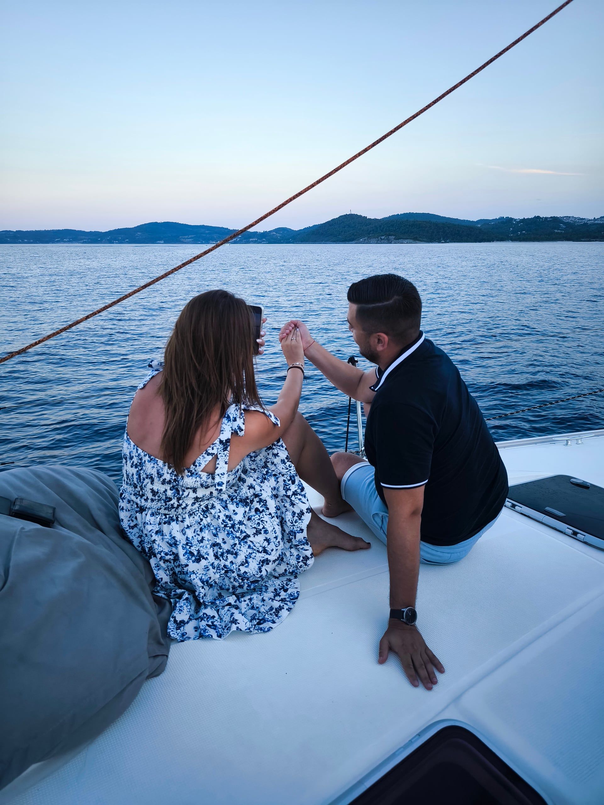 Couple sharing a toast on a sailing yacht’s bow at dusk
