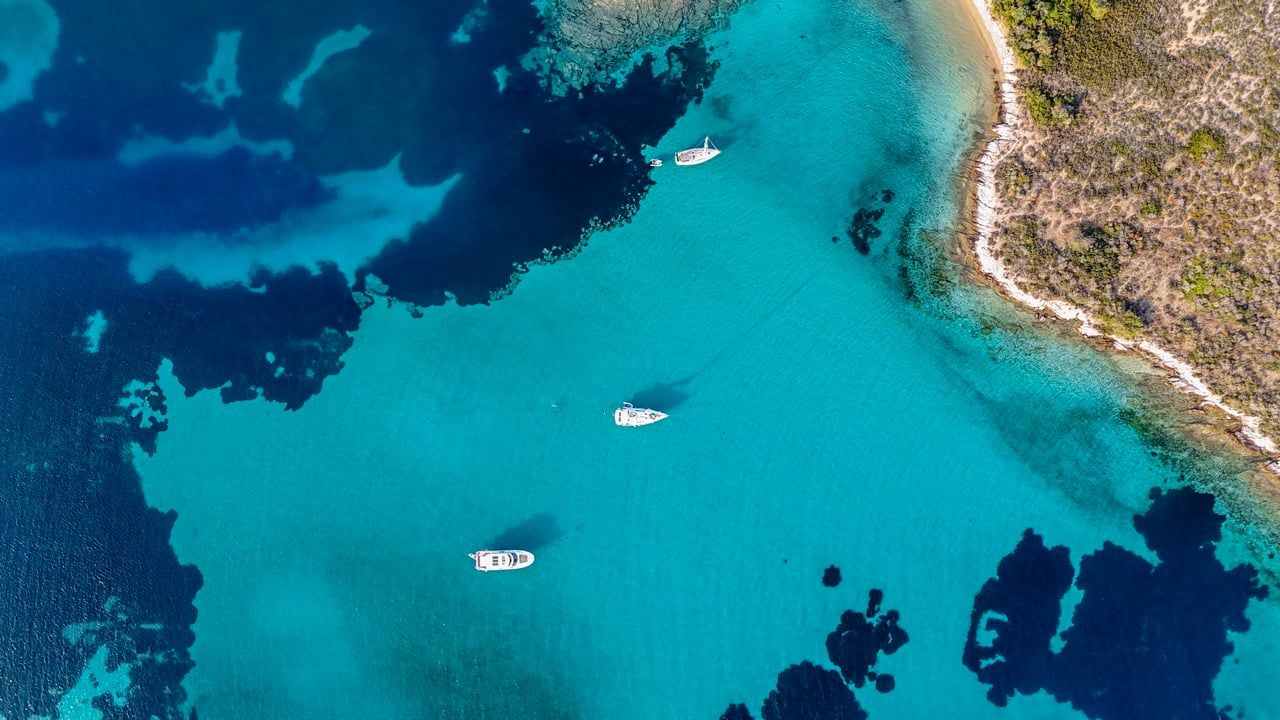 Three boats anchored over turquoise shallows off Diaporos on a Blue Lagoon cruise in Halkidiki