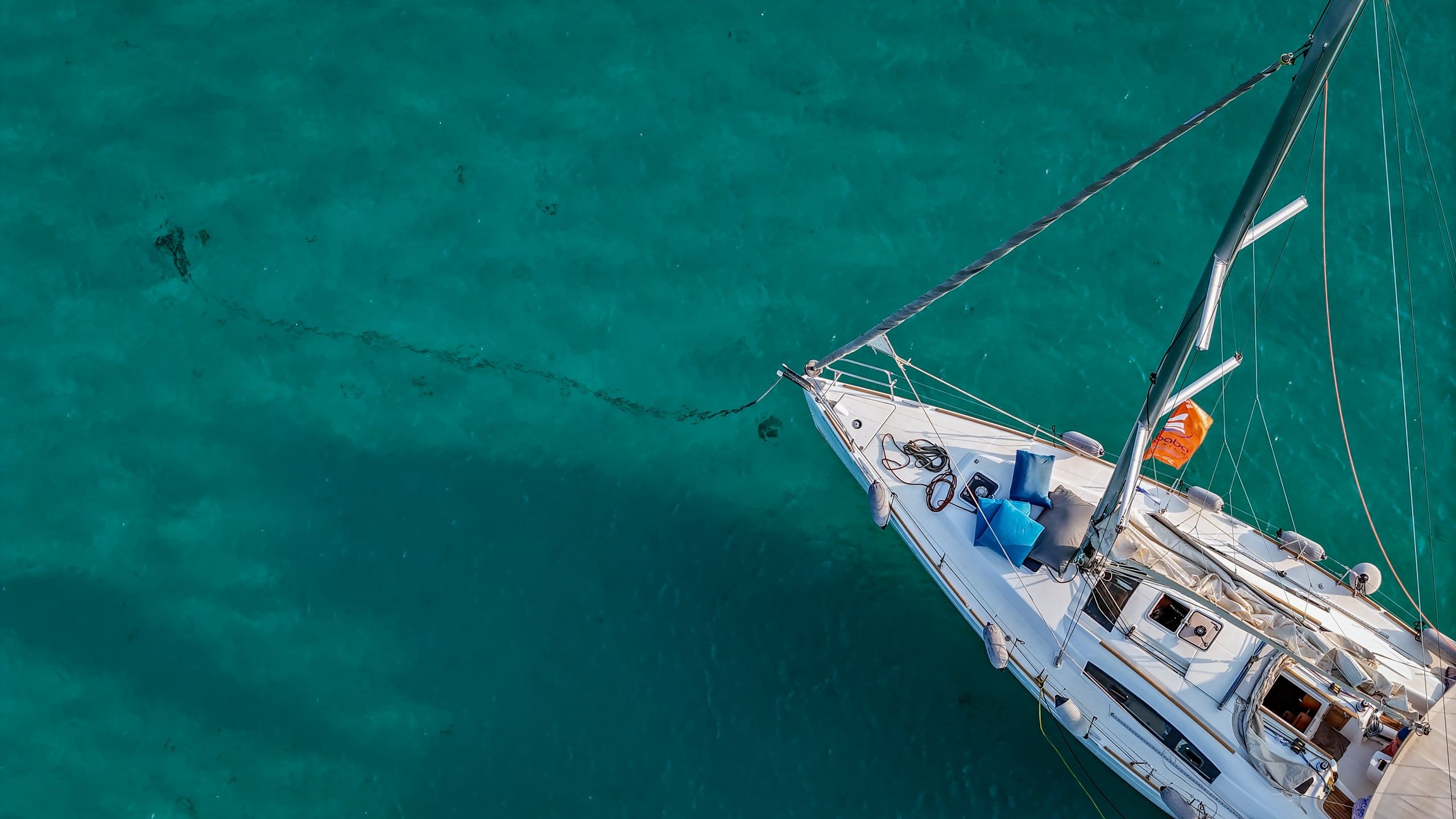 Bow of a sailing yacht at anchor over green-blue water off Diaporos, seen from above