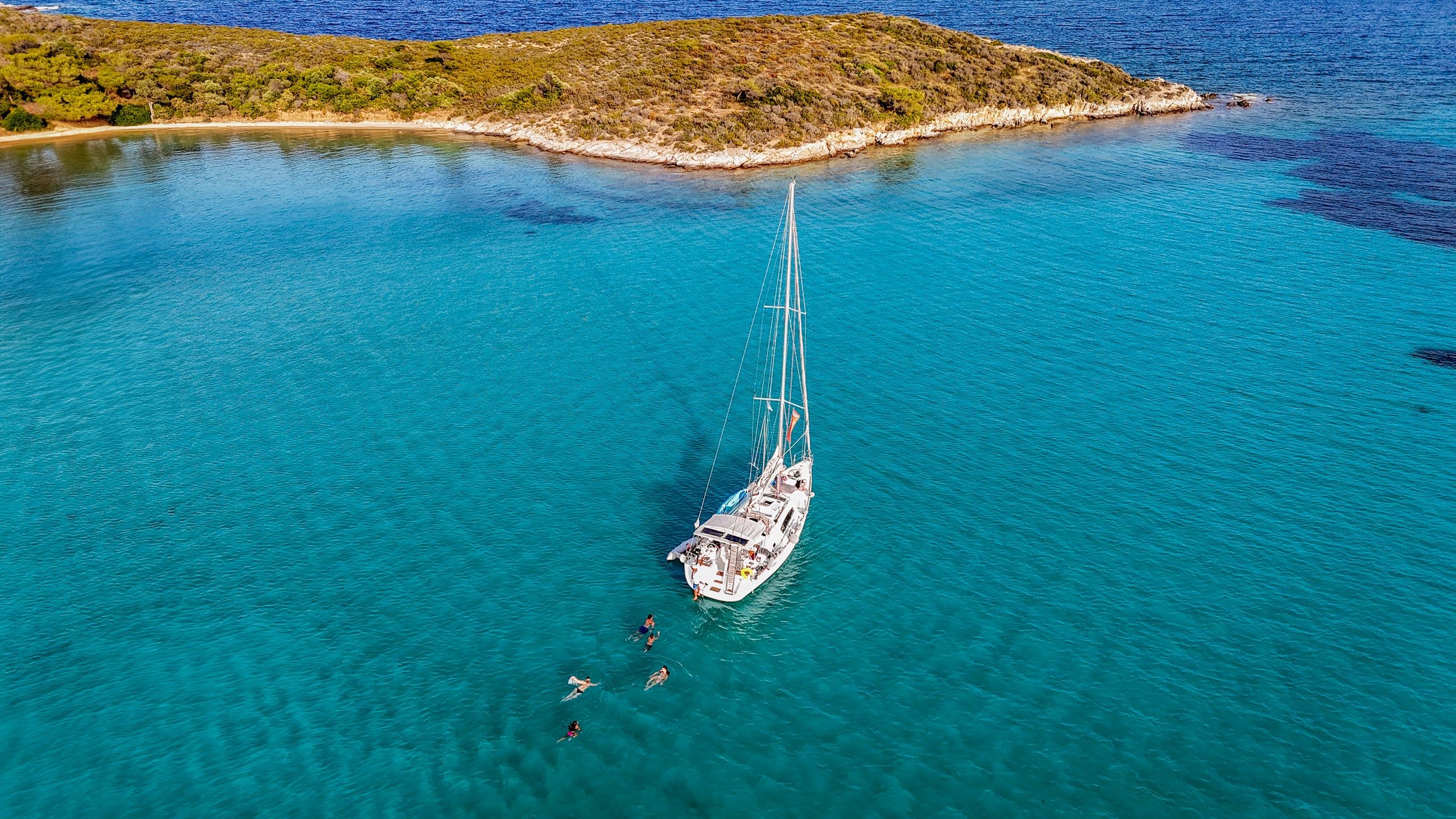 Sailing yacht anchored off a low islet near Diaporos, guests swimming in clear water