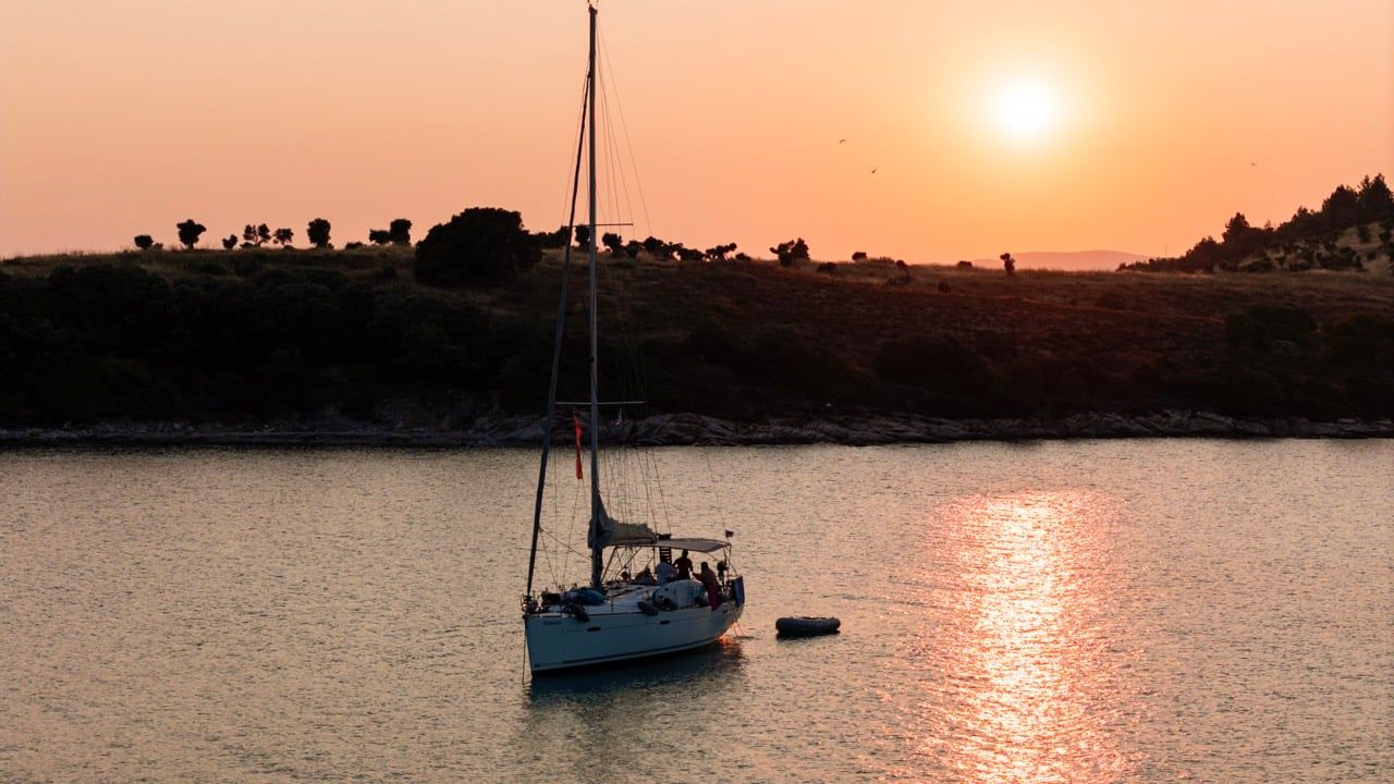 Sailing yacht anchored off Diaporos on a Blue Lagoon sunset cruise, a wooded island behind
