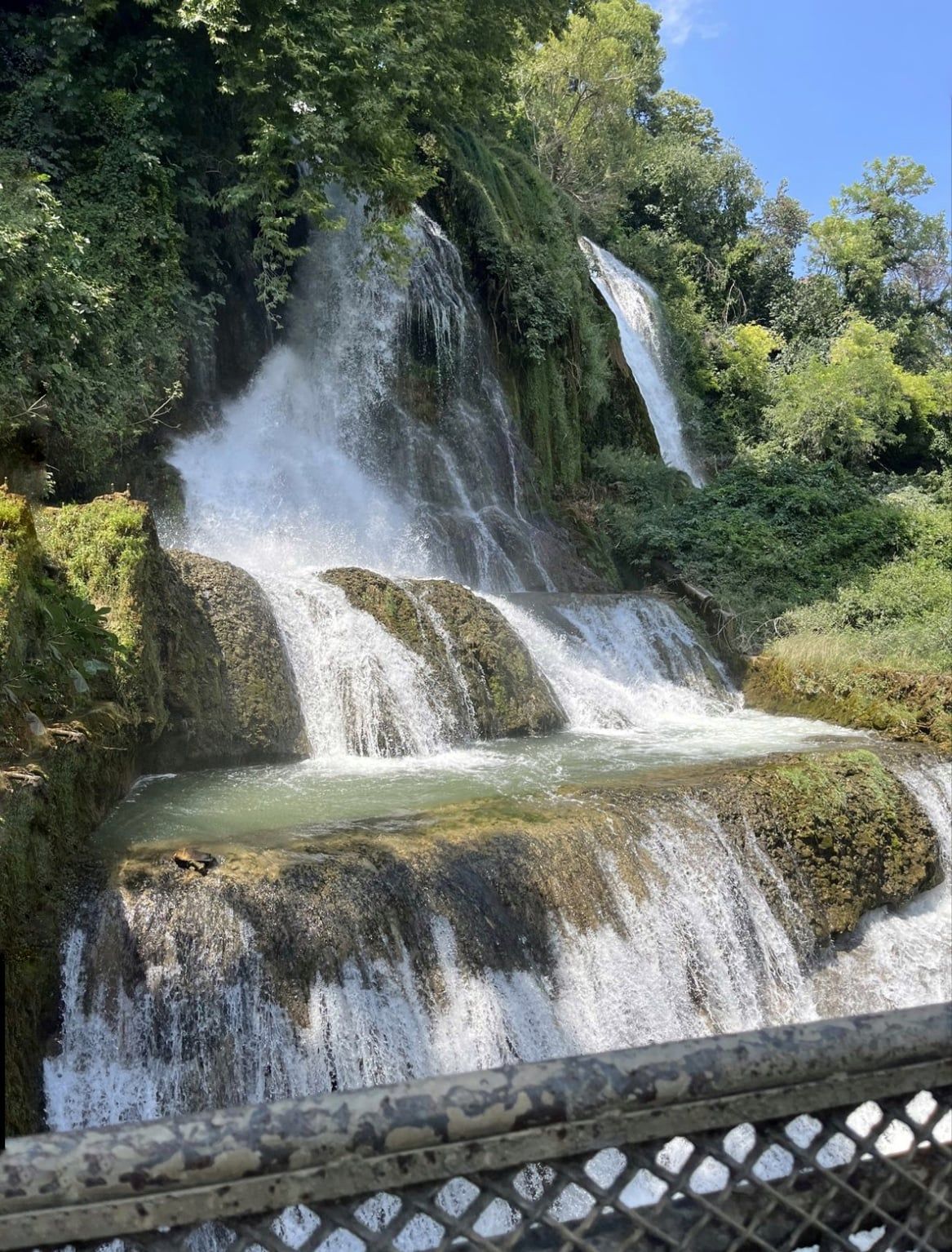 Water cascading over mossy rocks at the Edessa waterfalls, framed by green trees
