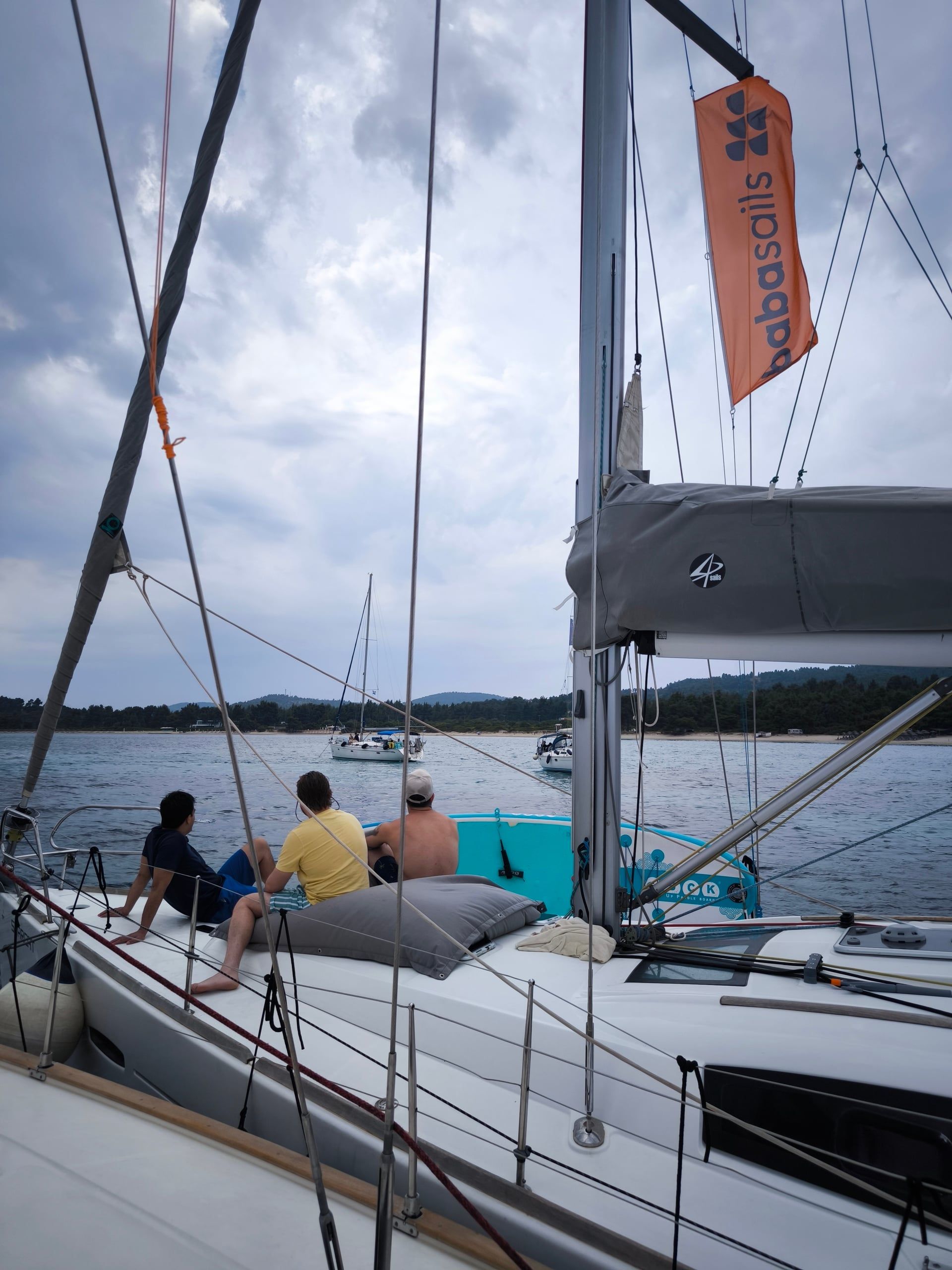 Friends sitting on the bow of a sailing yacht at anchor in a calm bay under clouds