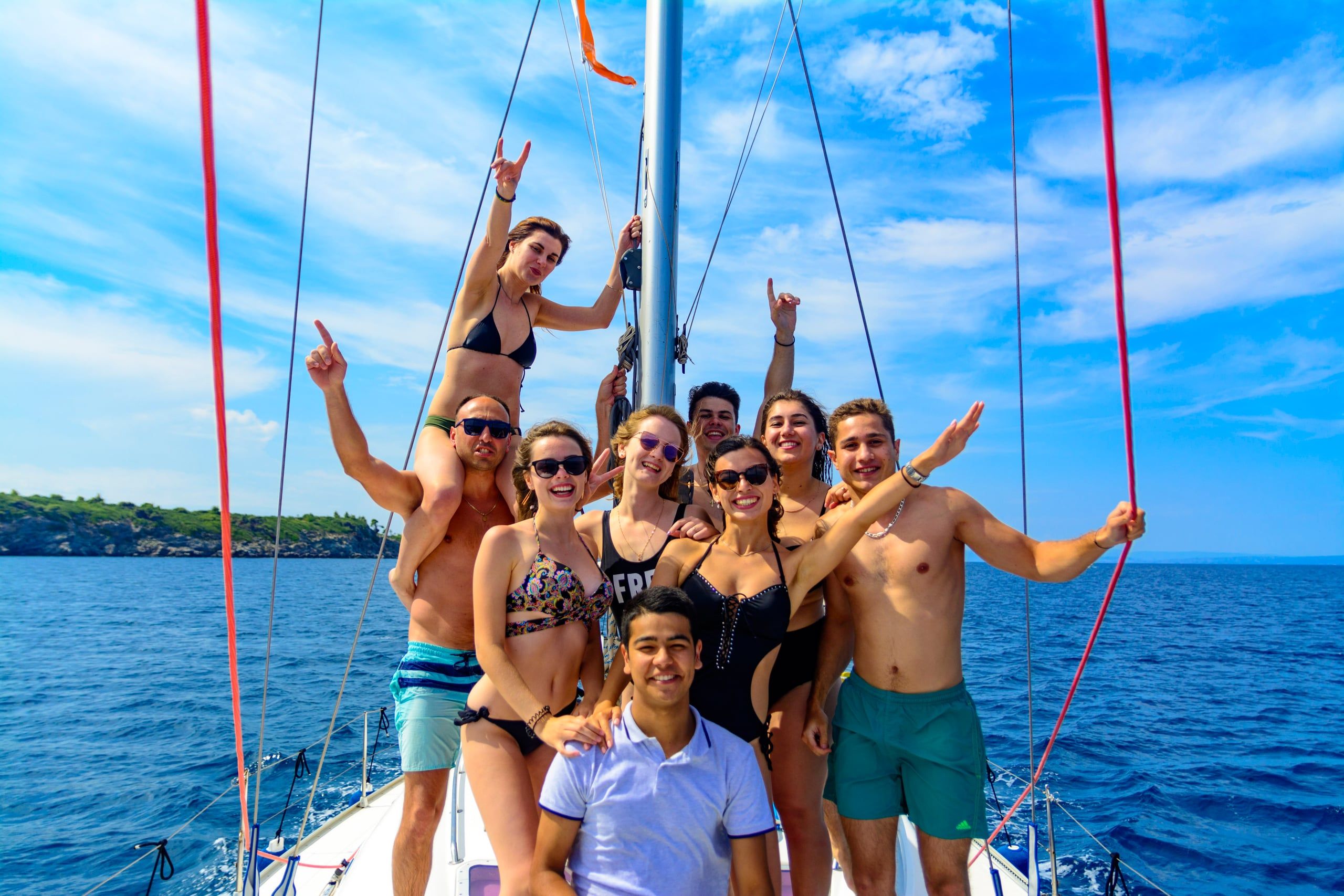Group of friends posing and cheering on the bow of a sailing yacht