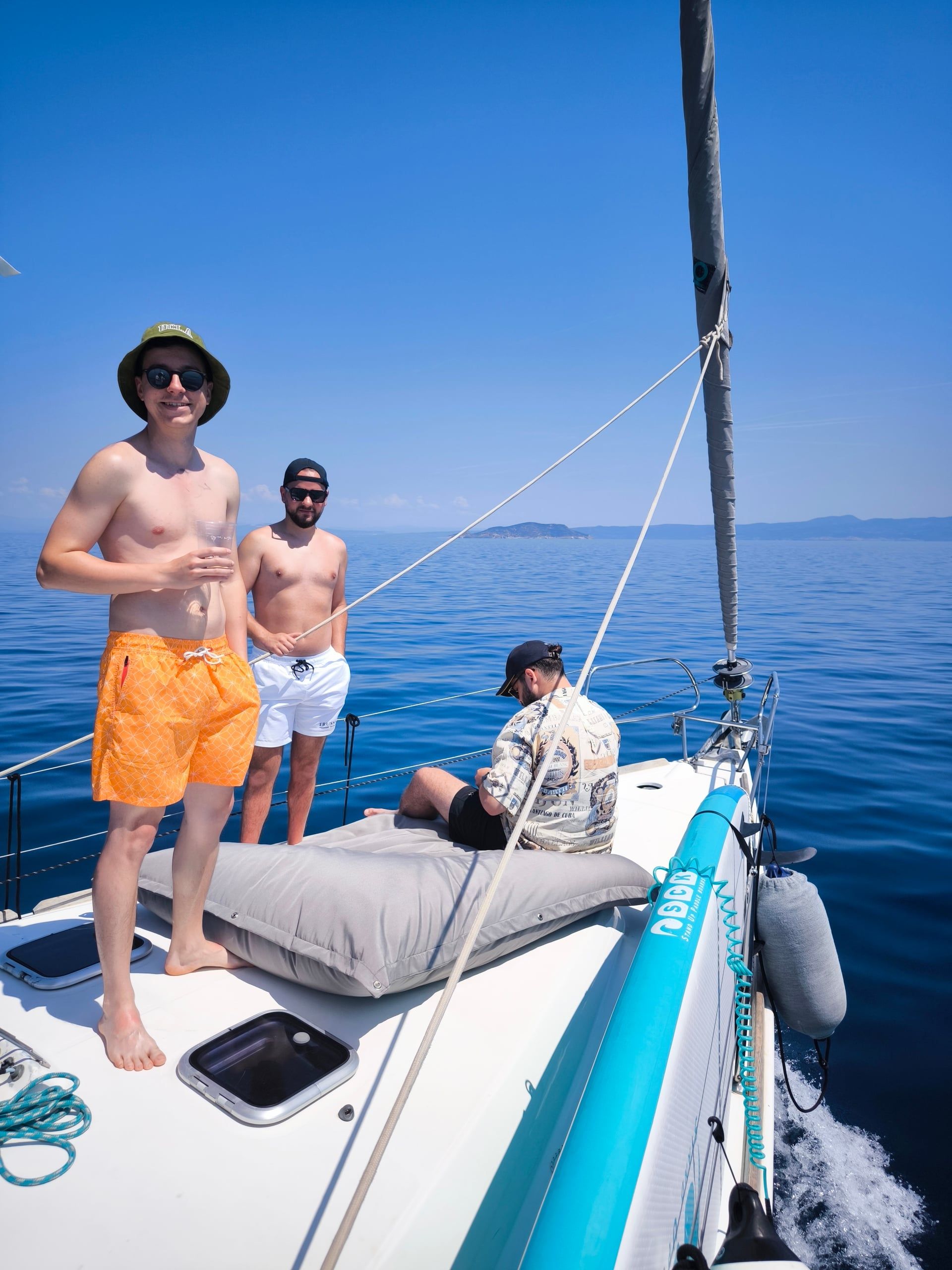 Friends standing on a sailing yacht’s bow on a calm blue sea