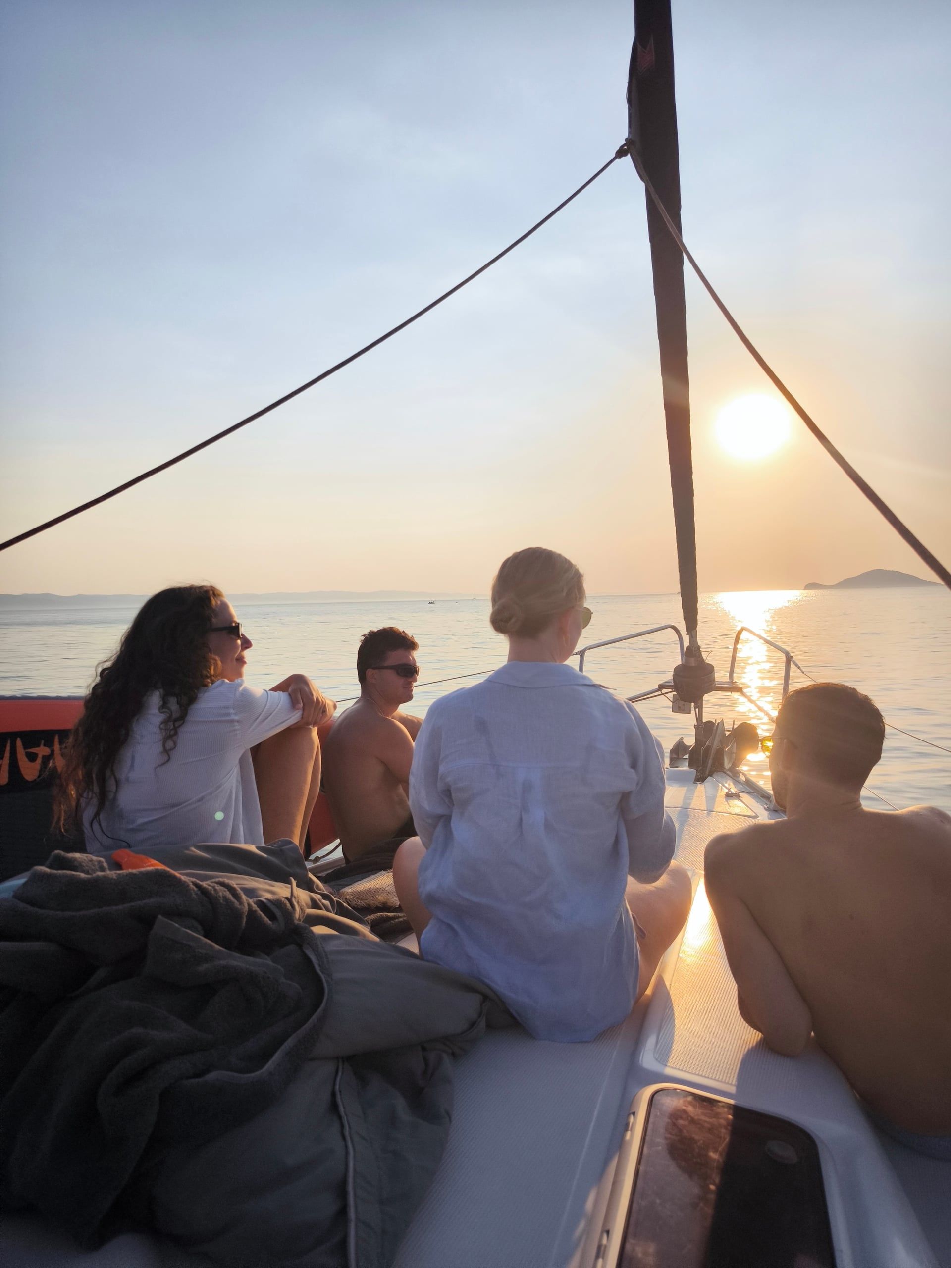 Friends sitting on a sailing yacht’s bow watching the sun set