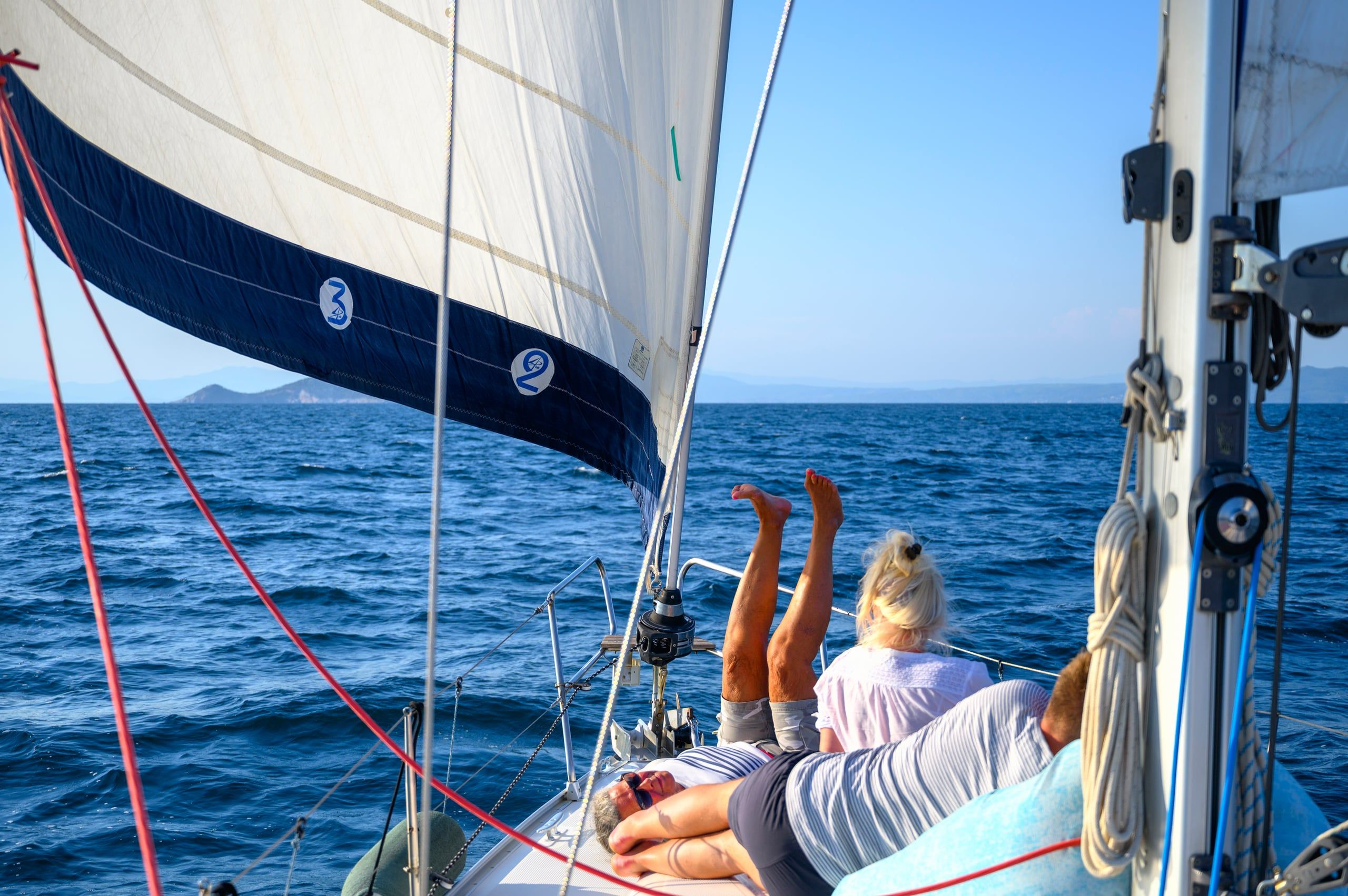 Guests lying on a sailing yacht’s deck under the genoa on open water