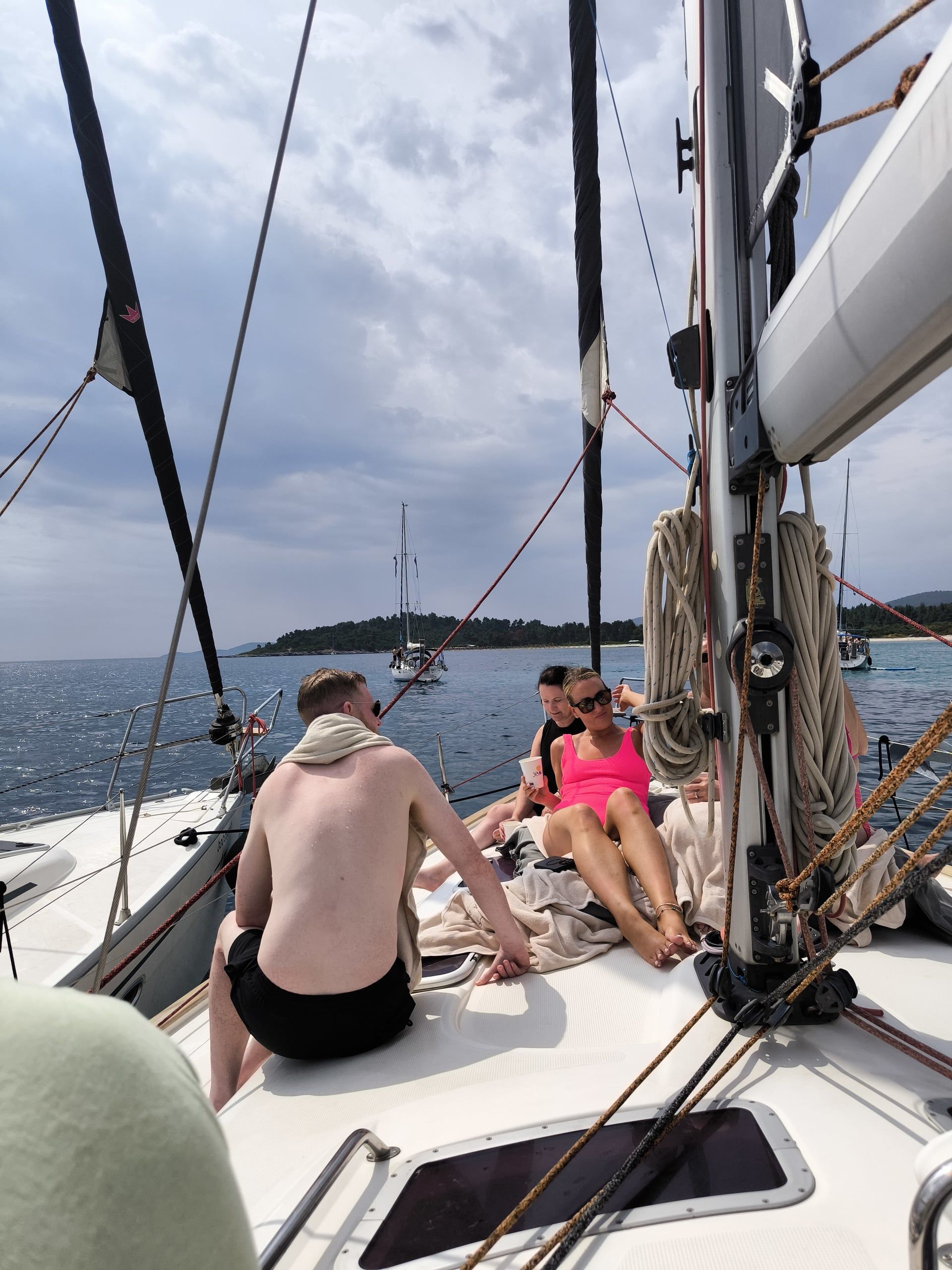 Guests relaxing on a sailing yacht’s bow under grey clouds