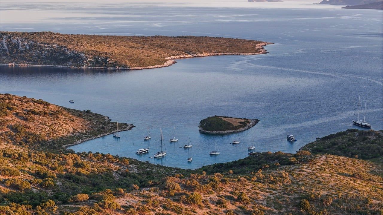 Sailing yachts anchored in a sheltered bay with an islet on Kyra Panagia at golden hour