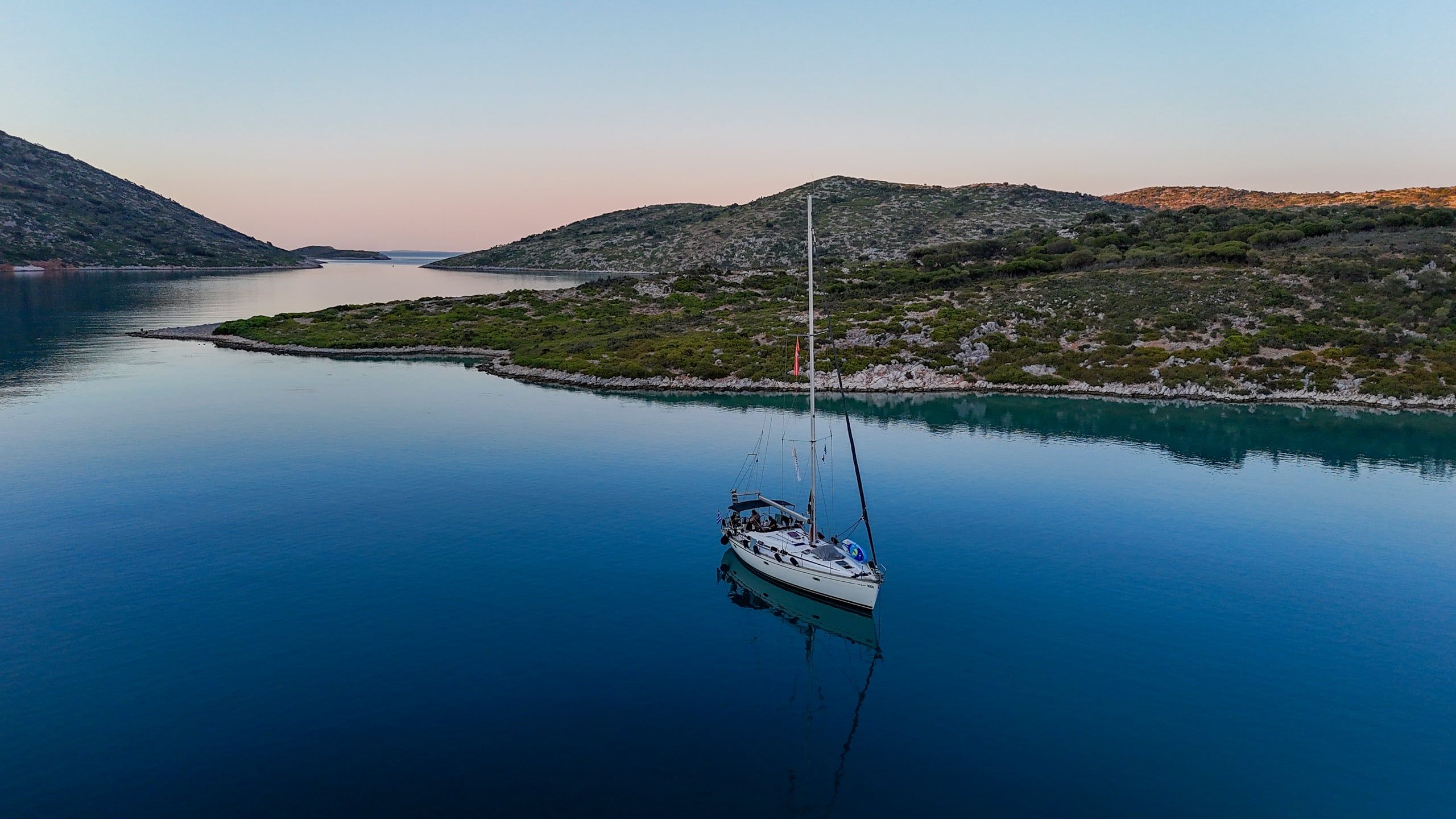 Sailing yacht at anchor on still water between low islands at dusk