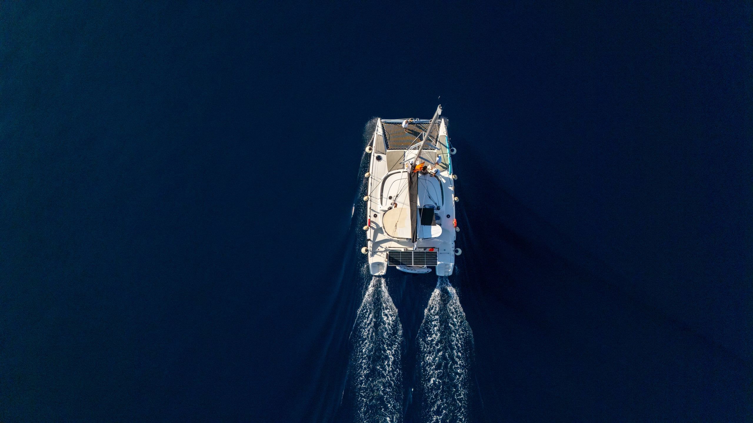 Catamaran motoring across deep blue water, seen from directly above