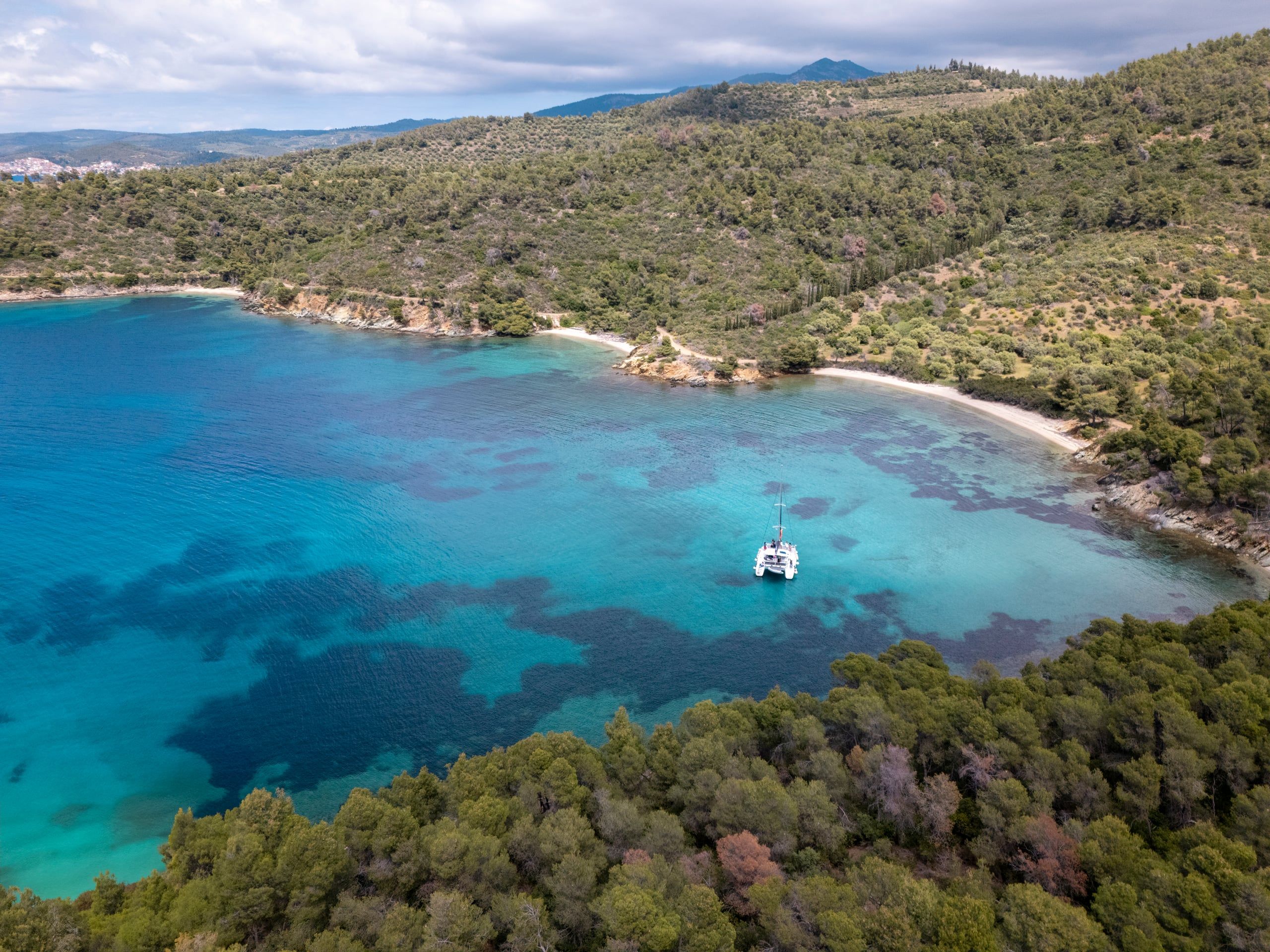 Catamaran anchored alone in a wide turquoise bay on a day sailing from Porto Carras