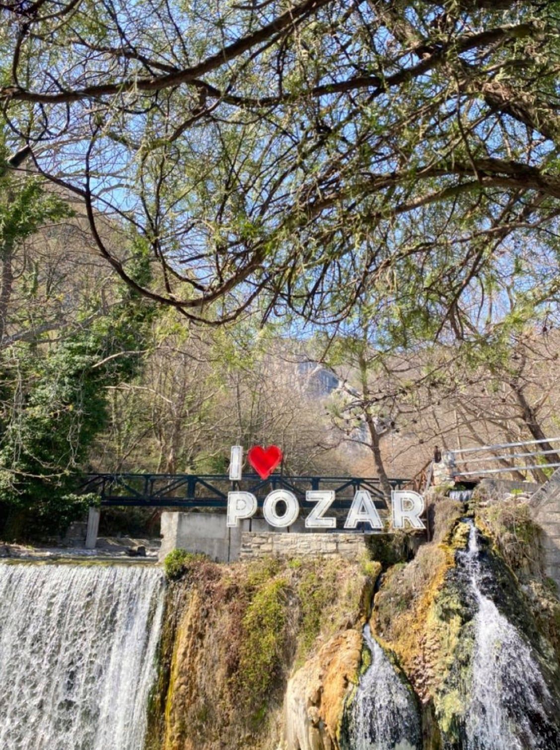 The I love Pozar sign above a waterfall and mossy rocks at the baths