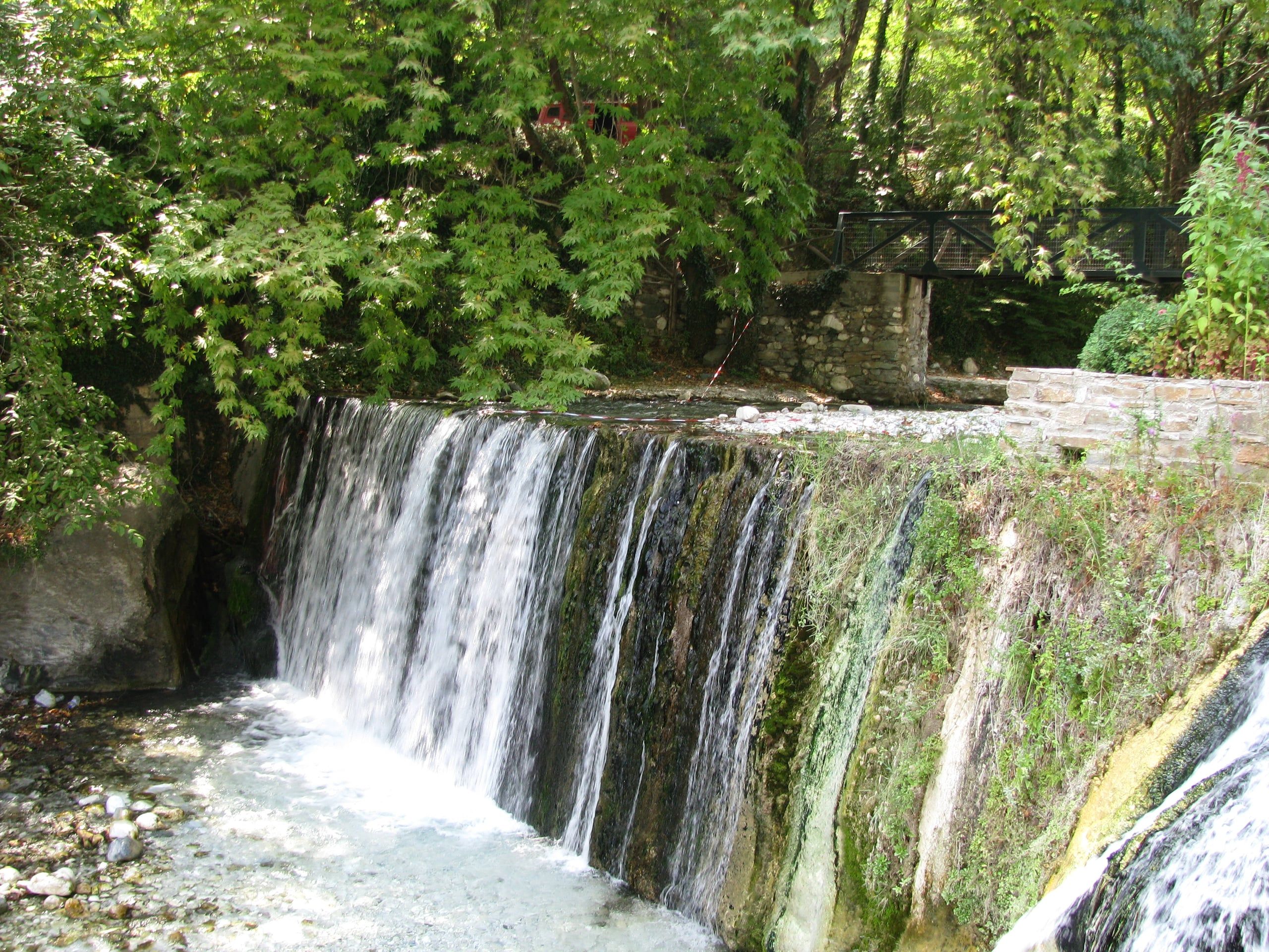 A wide waterfall pouring over mossy rock in the green gorge at Pozar