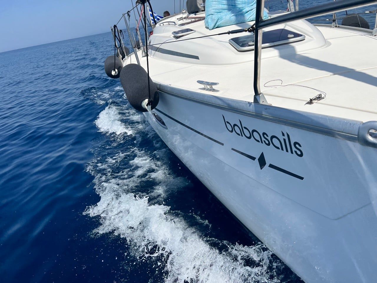 Bow of a sailing yacht cutting through deep blue water with a white wave