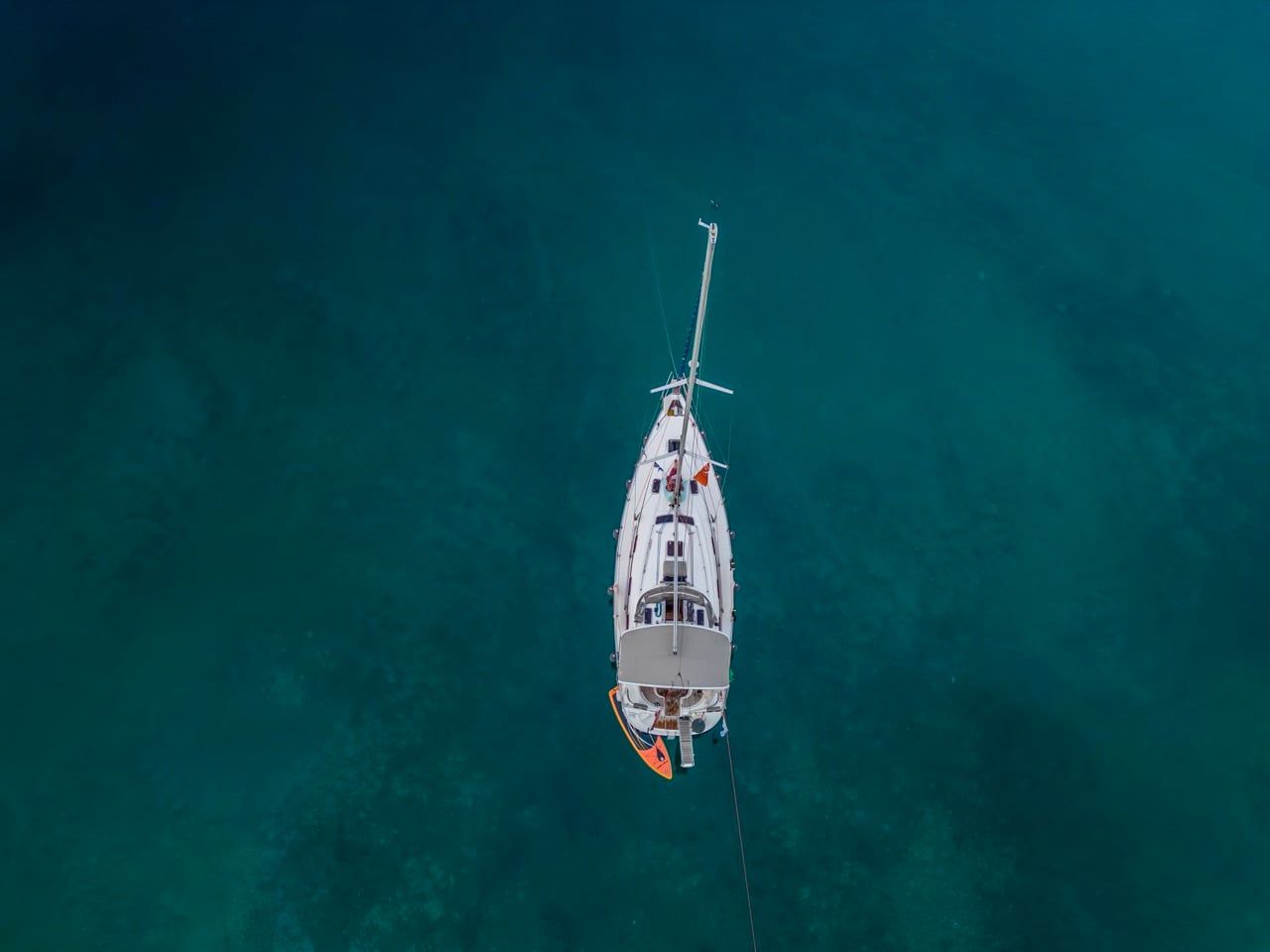 Sailing yacht at anchor in deep teal water, seen from directly above