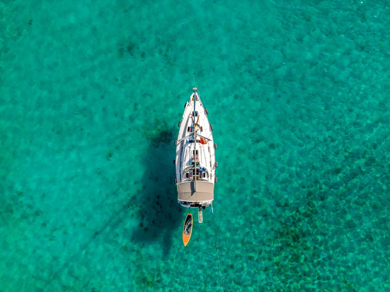 Sailing yacht at anchor with a paddleboard alongside, seen from directly above